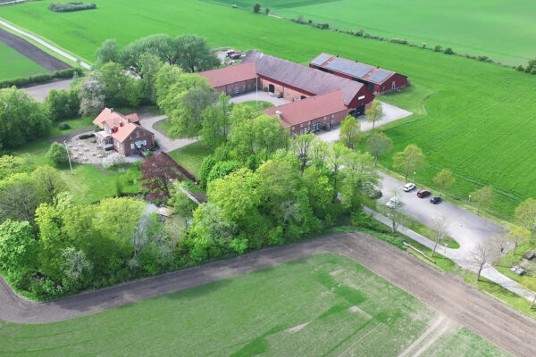 Gårdsbyggnader i tegel. Foto från ovan över gård och gröna fält.